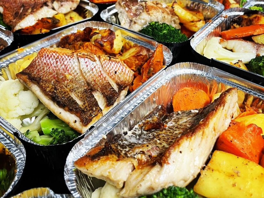 Boxed meals of grilled fish with roast vegetables lined up in foil trays
